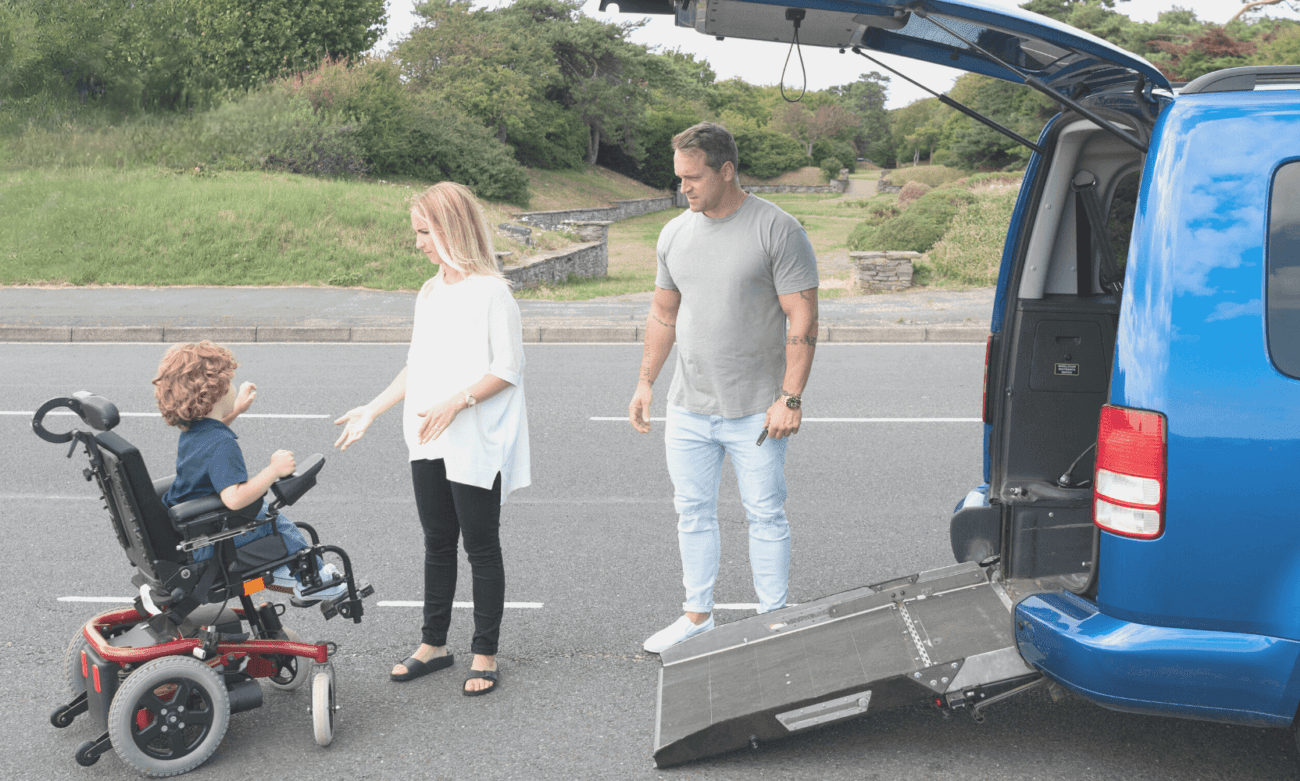 Familie mit behindertem Kind vor einem Auto mit Rollstuhlrampe